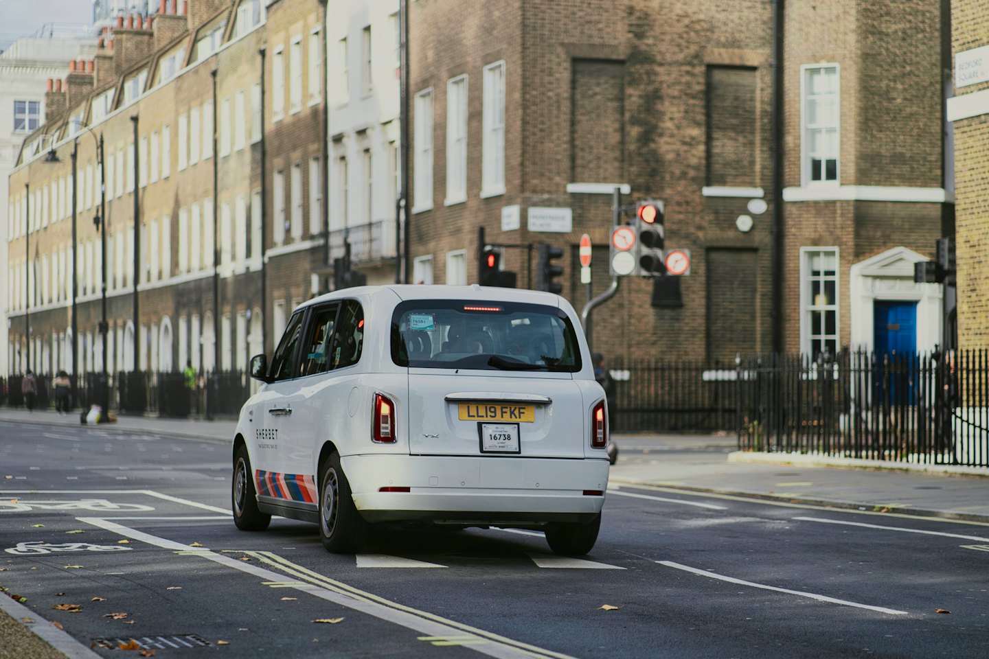 Angebot Moderner weißer Taxi fährt auf einer Stadtstraße davon.